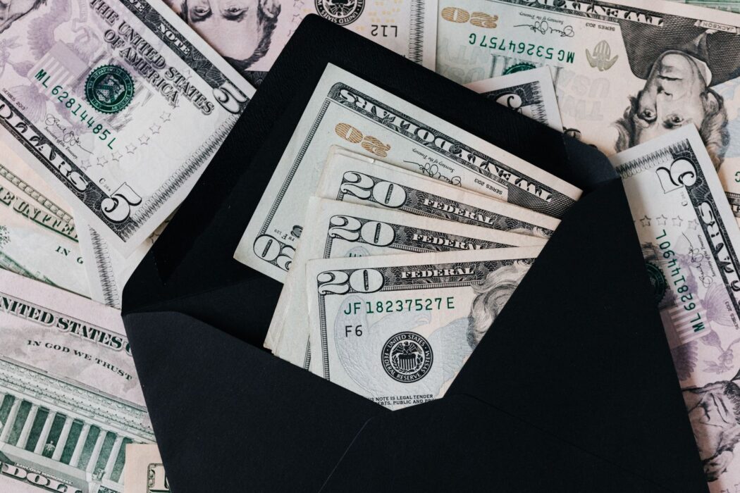 Enveloppe noire ouverte avec billets de dollars sur pile d'argent liquide