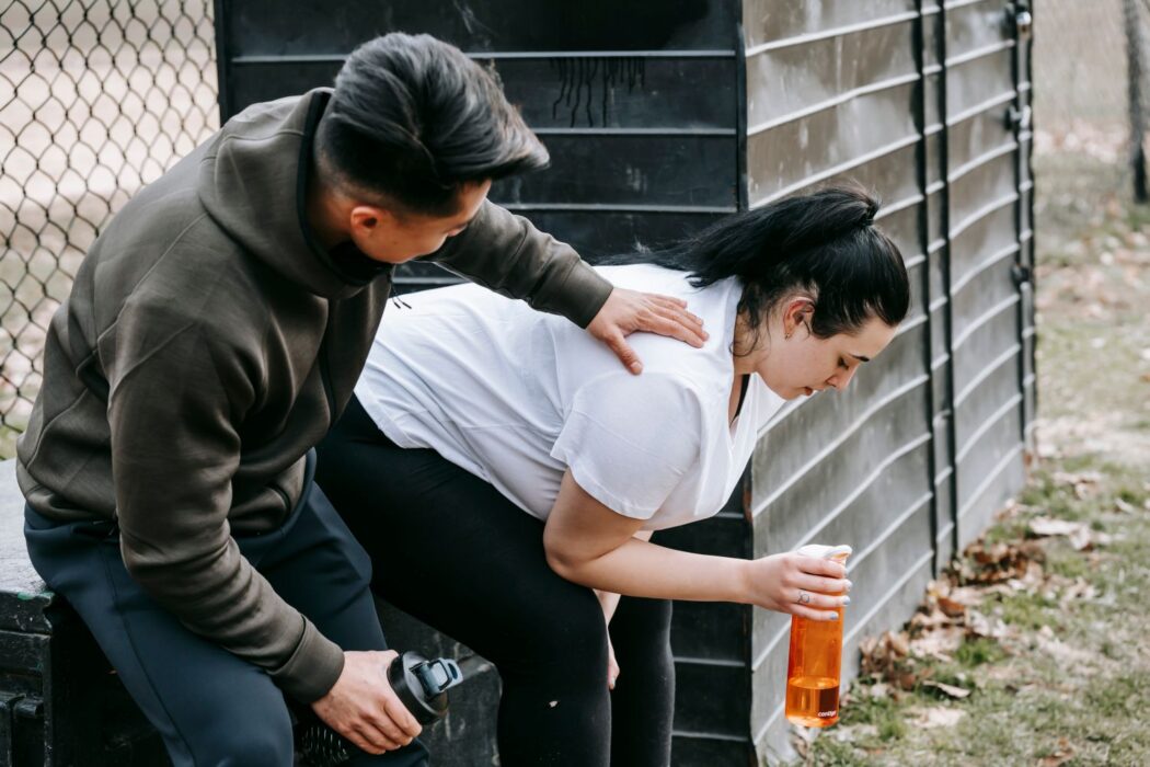 Homme touchant l'épaule d'une femme assise près d'un grillage avec bouteille d'eau, parc automnal