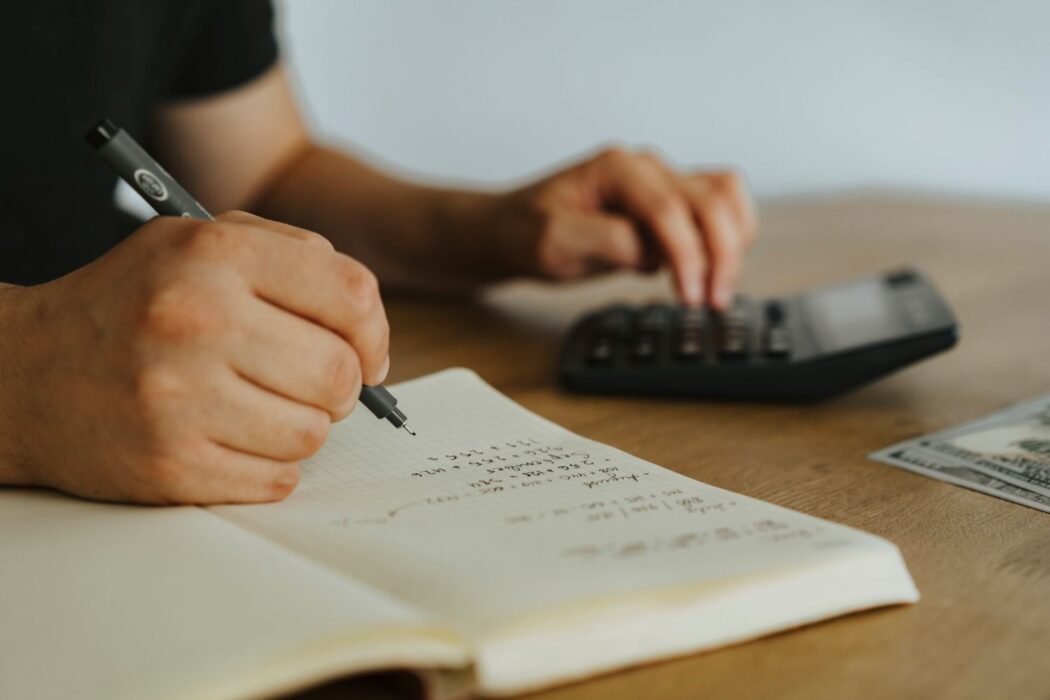 Mains écrivant des calculs dans un carnet avec une calculatrice, pour gérer sa bankroll hippique