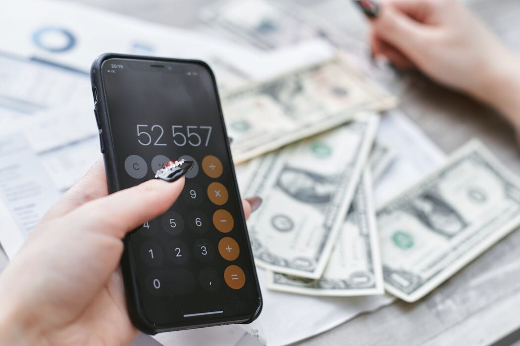 Mains utilisant une calculatrice sur smartphone près de billets pour gérer son budget de jeu