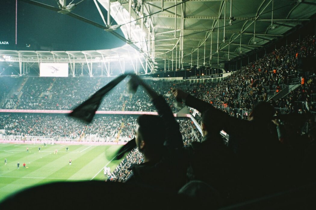 Match de foot nocturne dans un stade rempli, fans en liesse, pour parier