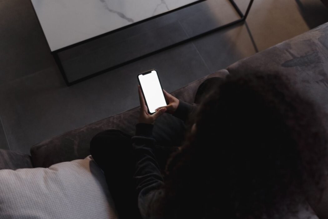 Personne assise sur un canapé tenant un smartphone à écran vide pour Neosurf